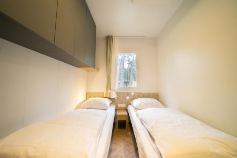 Twee eenpersoonsbedden in een heldere kamer met raam in Thor Cottage, Hoge Kempen Lodge, België.