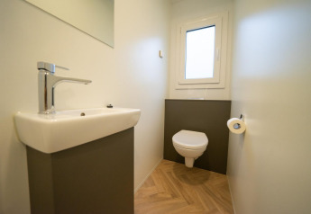 Baño moderno y minimalista en Thor Cottage, Hoge Kempen, Bélgica, con inodoro suspendido y lavabo pequeño.