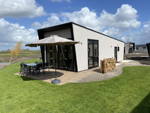 Just Nature Light lodge met modern design, buitenterras met stoelen, parasol en stapel hout op groene grasmat.