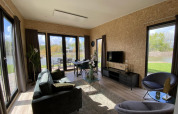 Moderne opholdsstue i Just Nature Light-lodgen, The IJssel Islands, med store vinduer og udsigt til natur.