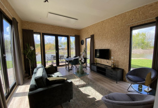 Moderne woonkamer in Just Nature Light lodge op de IJssel Eilanden, Nederland, met grote ramen en uitzicht.