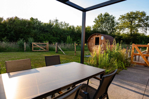 Buiteneettafel met stoelen en uitzicht op een sauna en tuin bij Hofparken Wiltershaar, Gelderland.