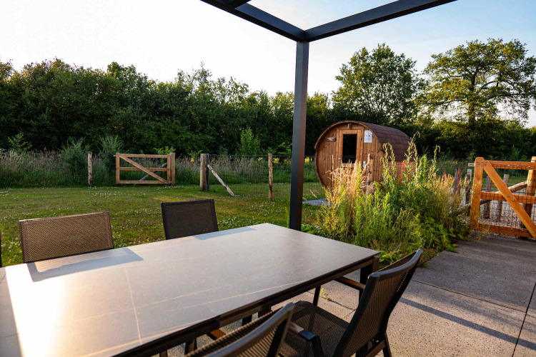 Tavolo da pranzo all’aperto con sedie e vista su sauna e giardino a Hofparken Wiltershaar, Gelderland.