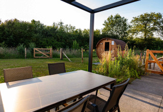 Tavolo da pranzo all’aperto con sedie e vista su sauna e giardino a Hofparken Wiltershaar, Gelderland.