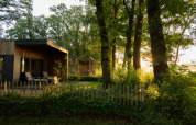 Moderne hytte i træ ved Hofparken Wiltershaar, omgivet af grønne træer og aftenlys i Gelderland.