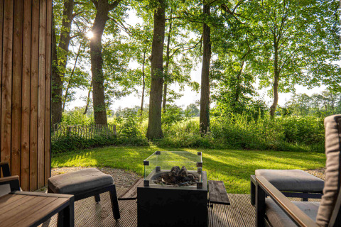 Zicht vanaf een terras met comfortabele stoelen en vuurkorf op het groen bij Hofparken Wiltershaar.