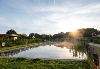 Solopgang over en fredelig dam omgivet af træer og ferieboliger ved Hofparken Wiltershaar, Gelderland.