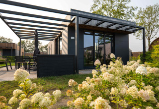 Moderne feriebolig med store vinduer og udvendig terrasse, omgivet af blomster i Hofparken De Bergvennen.