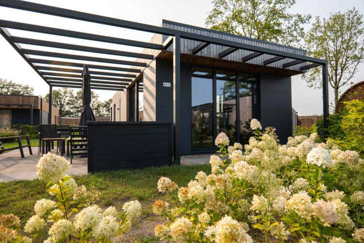 Moderne feriebolig med store vinduer og udvendig terrasse, omgivet af blomster i Hofparken De Bergvennen.