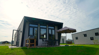 Moderne lodge bij Just Nature met terras, parasol, barbecue en tuinstoelen op de grasweide.