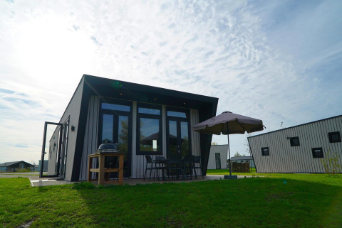 Moderne lodge bij Just Nature met terras, parasol, barbecue en tuinmeubilair op het gras.
