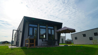 Moderne lodge bij Just Nature met terras, parasol, barbecue en tuinstoelen op de grasweide.