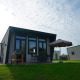 Moderne hytte ved Just Nature med terrasse, parasol og grill under en overskyet himmel.