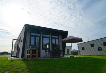 Moderne lodge bij Just Nature met terras, parasol, barbecue en tuinmeubilair op het gras.