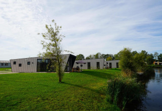 Moderne Just Nature lodge aan een vijver, omgeven door grasvelden en bomen onder een open lucht.