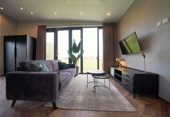 Salon moderne du lodge Just Nature aux Îles IJssel, Pays-Bas, avec canapé, TV et grandes fenêtres sur le jardin.
