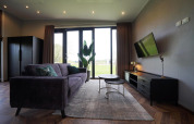 Salon moderne du lodge Just Nature aux Îles IJssel, Pays-Bas, avec canapé, TV et grandes fenêtres sur le jardin.