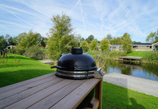 Parrilla cerámica negra en mesa de madera con vistas al lago y cabañas en Just Nature, Islas IJssel.