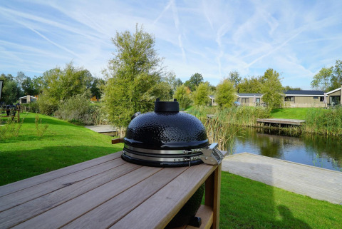 Black ceramic grill on wooden table overlooking pond and lodges at Just Nature, IJssel Islands, Netherlands.
