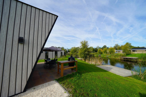 Moderne lodge Just Nature bij de IJssel Islands in Nederland met terras, water en groene natuur rondom.