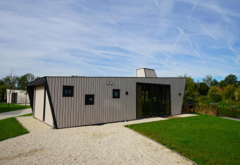 Modern lodge called Just Nature with light wood panels at The IJssel Islands, Netherlands, surrounded by greenery.
