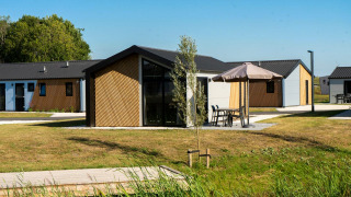 Buitenbeeld van Velthorst lodge met hedendaagse huisjes, groene gazons en terrasmeubilair met parasols.