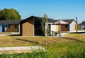 Buitenaanzicht van Velthorst lodge met moderne vakantiehuisjes, groene gazons en tuinmeubilair met parasols.