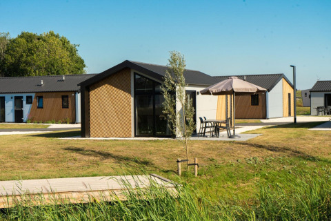 Vista exterior de la lodge Velthorst con cabañas modernas, césped verde y mesas de jardín bajo sombrillas.