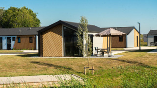 Vista exterior de la lodge Velthorst con cabañas modernas, césped verde y mesas de jardín bajo sombrillas.