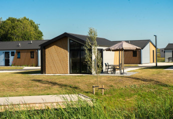 Buitenbeeld van Velthorst lodge met hedendaagse huisjes, groene gazons en terrasmeubilair met parasols.