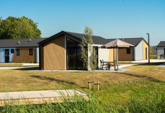 Vista exterior de la lodge Velthorst con cabañas modernas, césped verde y mesas de jardín bajo sombrillas.