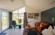 Woonkamer in de Velthorstlodge op de IJssel-eilanden met grote ramen en een bruine sofa.