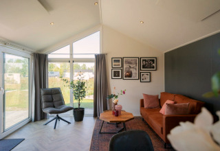 Woonkamer in de Velthorst-lodge op de IJssel Eilanden, met grote ramen en een bruine bank.