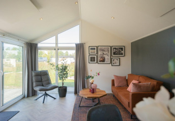 Woonkamer in de Velthorstlodge op de IJssel-eilanden met grote ramen en een bruine sofa.