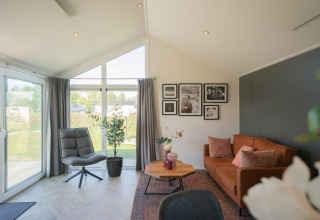 Wohnzimmer in der Velthorst-Lodge auf den IJssel-Inseln, mit großen Fenstern und braunem Sofa.