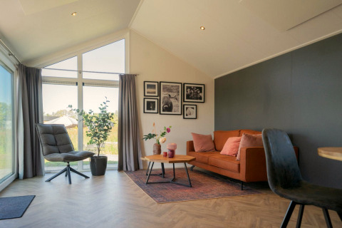 Lichte woonkamer in de Velthorst lodge op de IJssel Eilanden, Nederland, met bank, stoel en grote ramen.