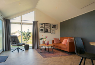 Lichte woonkamer in de Velthorst lodge op de IJssel Eilanden, Nederland, met bank, stoel en grote ramen.