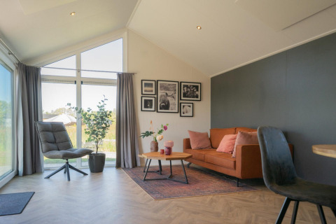 Lichte woonkamer in de Velthorst lodge op de IJssel Eilanden, Nederland, met bank, stoel en grote ramen.