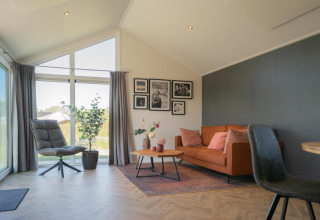 Zona living luminosa nella lodge Velthorst alle Isole IJssel, Paesi Bassi, con divano, poltrona e grandi finestre.