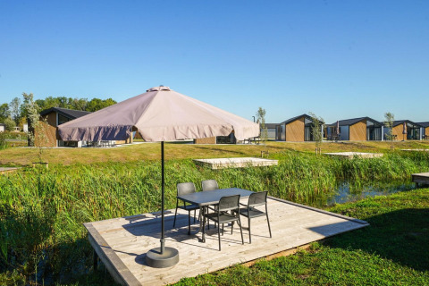 Terraza exterior con sombrilla y mesa en Lodge Velthorst, The IJssel Islands, Países Bajos, con cabañas al fondo.
