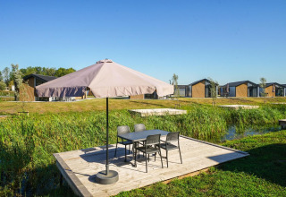 Terraza exterior con sombrilla y mesa en Lodge Velthorst, The IJssel Islands, Países Bajos, con cabañas al fondo.