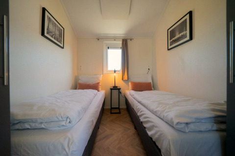 Velthorst lodge-kamer op de IJssel Eilanden, Nederland, met twee eenpersoonsbedden, raam en kunstwerken.