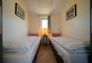 Velthorst lodge-kamer op de IJssel Eilanden, Nederland, met twee eenpersoonsbedden, raam en kunstwerken.