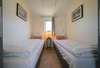 Habitación de la cabaña Velthorst en las Islas IJssel, Países Bajos, con dos camas, ventana y cuadros.