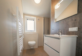 Modern badkamer met zwevend toilet, wit wastafelmeubel en spiegel in Velthorst Lodge, IJssel Eilanden.