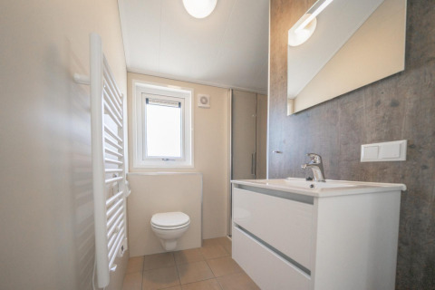 Modernes Badezimmer mit Wandtoilette, weißem Waschbecken und Spiegel in der Velthorst Lodge, IJsselinseln.
