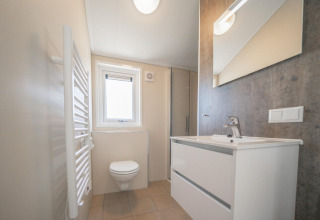 Baño moderno con inodoro mural, lavabo blanco y espejo en Velthorst Lodge en las Islas IJssel.