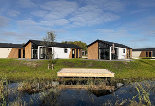 Moderne Velthorst-lodge bij De IJssel Eilanden in Nederland, met water, gras en blauwe lucht op de achtergrond.