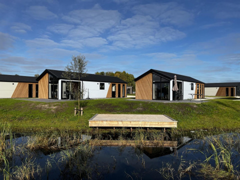 Moderne Velthorst-Lodges an den IJssel-Inseln in den Niederlanden, mit Wasser, Rasen und blauem Himmel.