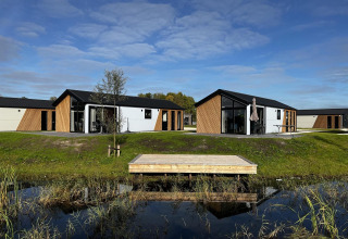 Moderne Velthorst-hytter ved The IJssel Islands i Holland, med vand, græs og blå himmel i baggrunden.